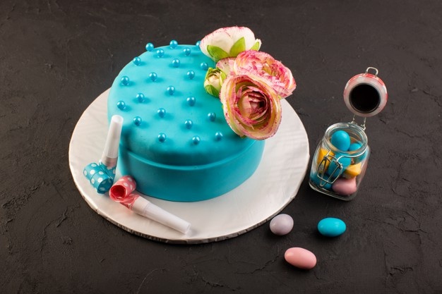 Um bolo de aniversário de frente para o azul com flores no topo e decorações