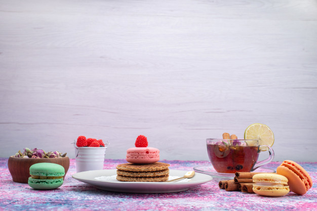 Vista frontal de biscoitos e macarons com chá e canela na mesa de luz Foto gratuita